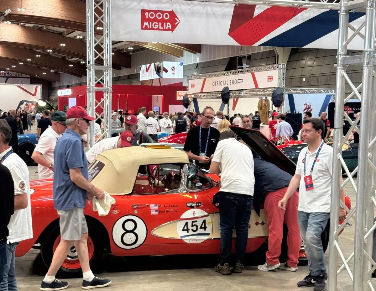 A red 1957 Corvette with race number 454, surrounded by its crew at the 1000 Miglia in Brescia