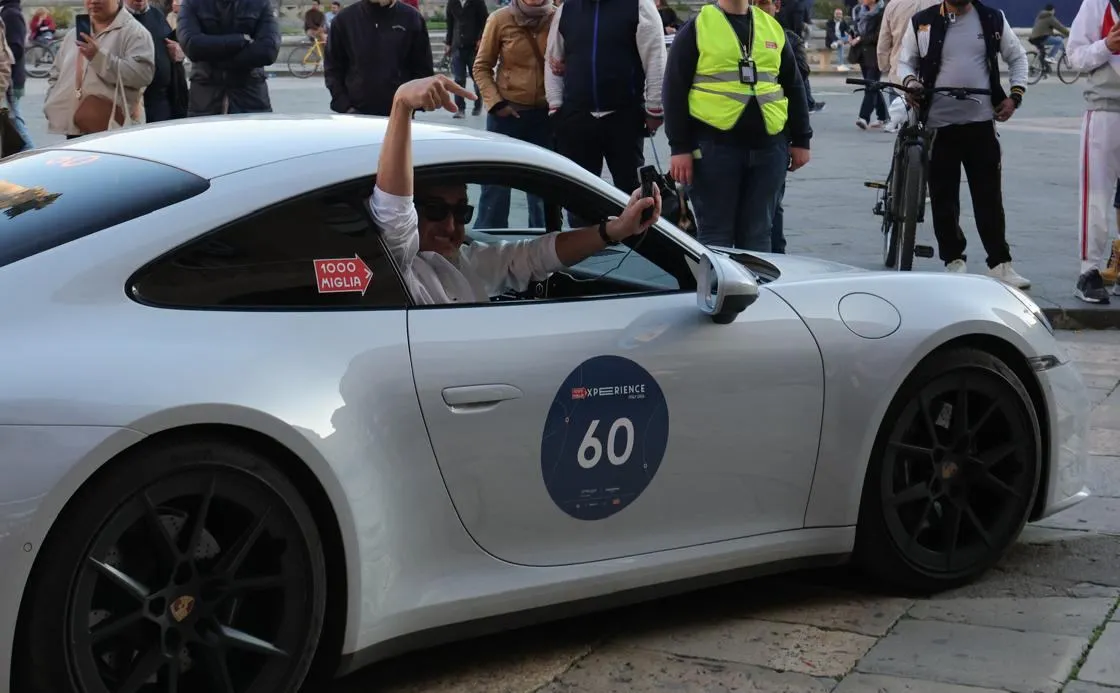 The navigator of car 60 leaning out of the window, pointing at the Crono107 joystick in his other hand, in a crowded Italian piazza