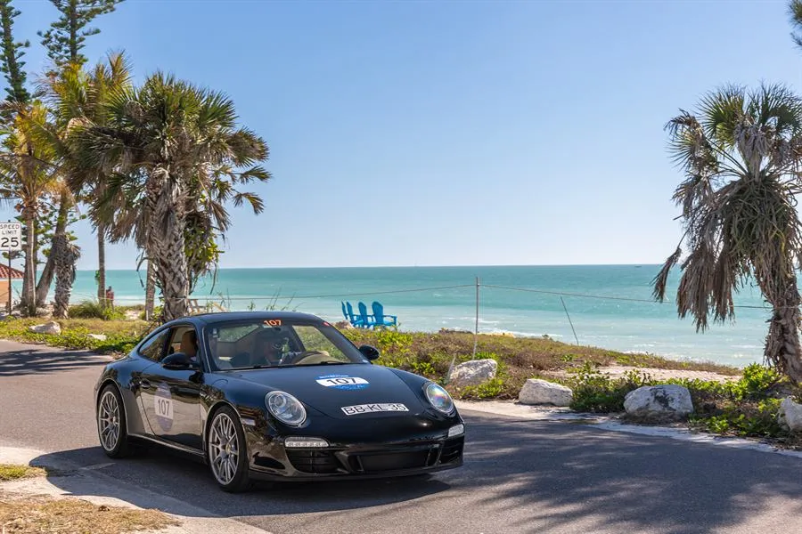 Car 107, a black Porsche 911, on a coastal road lined with palm trees in Florida